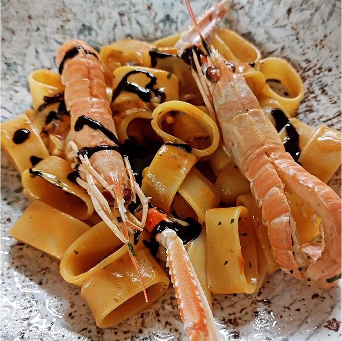 Piatto di calamarata con scampi interi e riduzione scura, servito su piatto chiaro.