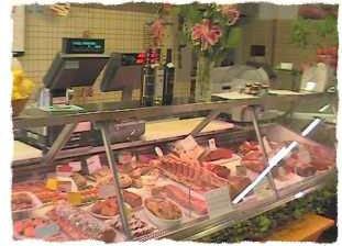 Banco frigo di una macelleria con carni e salumi esposti sui vassoi e bilancia sul retro