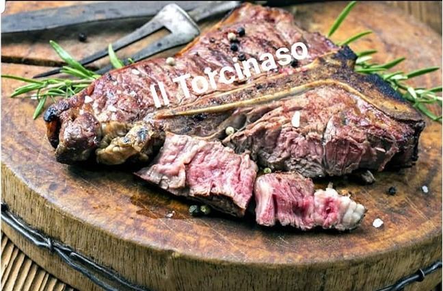 Bistecca alla fiorentina tagliata su tagliere di legno con rosmarino, sovrimpressa la scritta Il Torcinaso.