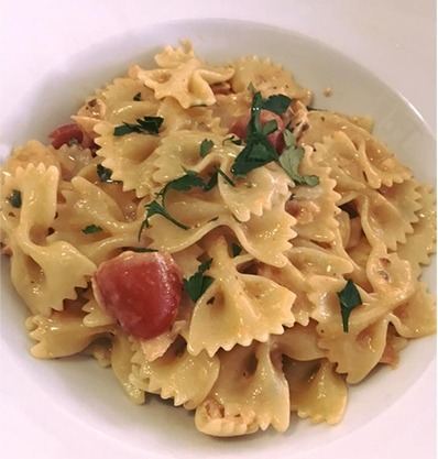 Piatto di farfalle con pomodorini e prezzemolo servito in una fondina bianca.