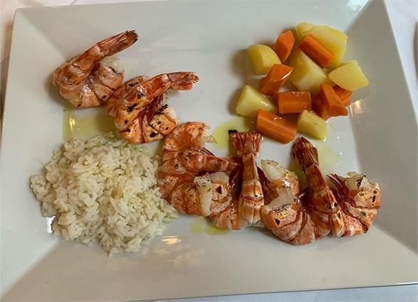Piatto quadrato con gamberoni alla griglia, riso bianco e cubetti di patate e carote.