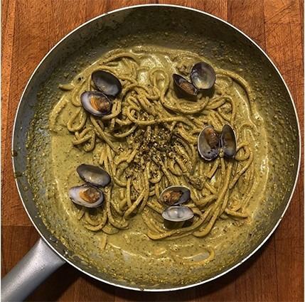 Padella vista dall'alto con pasta lunga mantecata in crema verde e vongole ancora nel guscio
