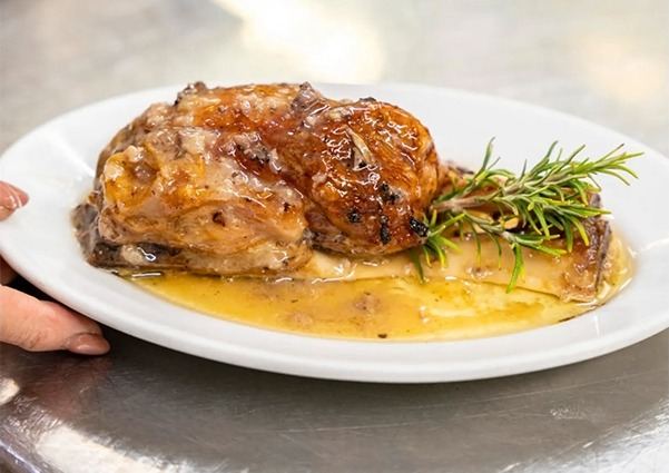 Piatto di carne brasata con salsa e rametto di rosmarino, servito su polenta.
