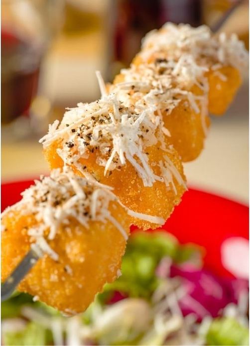 Spiedino di bocconcini fritti spolverati di formaggio grattugiato, servito sopra un'insalata.